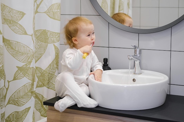 Un tout-petit assis sur le meuble du lavabo et se brosser les dents Routine d'hygiène quotidienne du matin