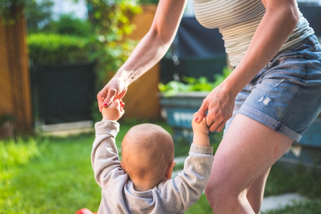 Tout-petit fait ses premiers pas en tenant la main de sa mère Gros plan par derrière