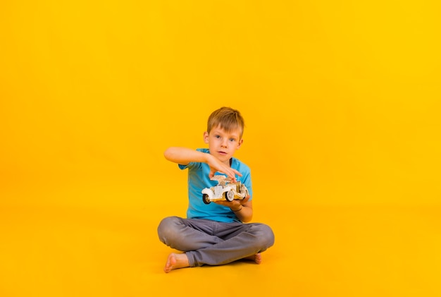 Le tout-petit garçon joue avec une voiture rétro blanche et regarde la caméra sur un fond jaune avec un espace pour le texte