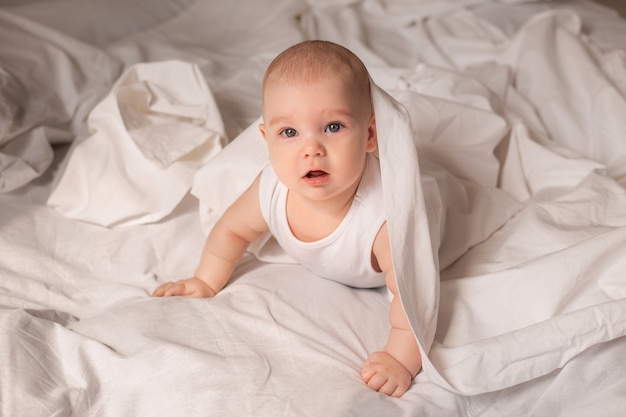 Tout-petit mignon en body blanc se trouve dans son lit avec une literie blanche