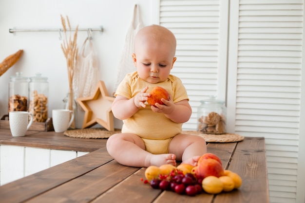 Tout-petit mignon mange des fruits dans la cuisine en bois à la maison