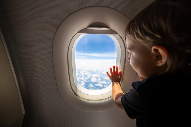 Tout-petit mignon pointe son doigt vers le ciel à travers le concept de premier vol de la fenêtre voyageant avec