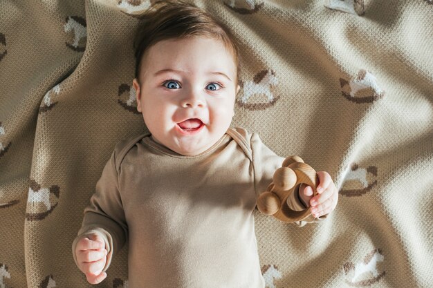 Photo tout-petit nouveau-né garçon souriant en body beige joue avec vue de dessus de jouet en bois