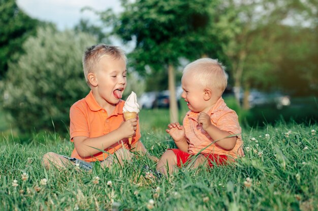 Photo un tout-petit pleure pendant que son frère mange de la crème glacée sur l'herbe.