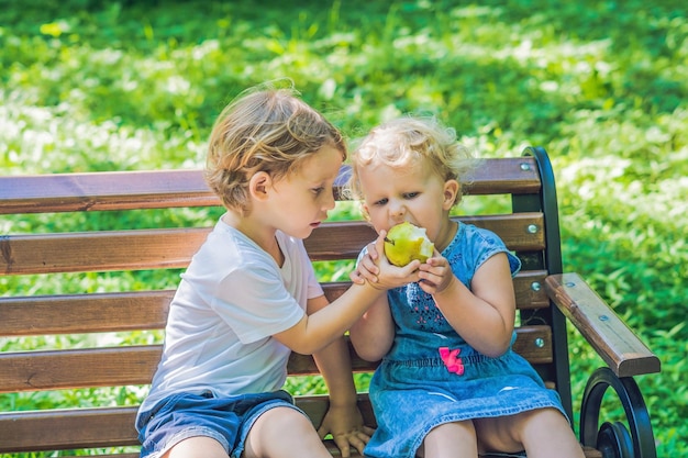 Tout-petits garçon et fille assis sur un banc au bord de la mer et mange une pomme