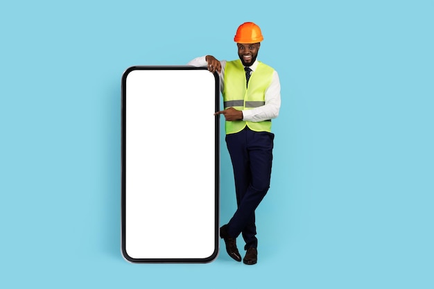 Tout pour la construction heureux ingénieur noir pointant sur un grand écran de smartphone vierge