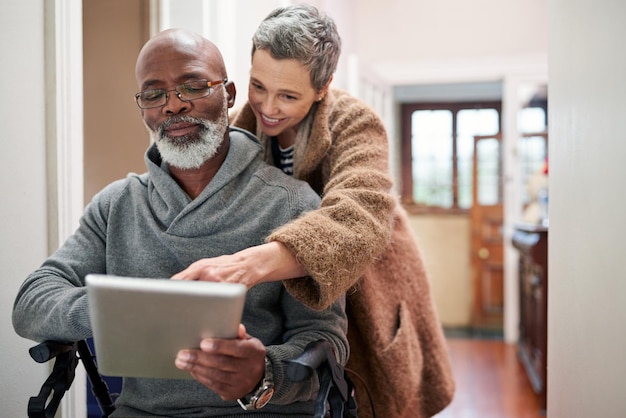 Tout ce qui compte, c'est qu'ils étaient ensemble Photo recadrée d'un couple de personnes âgées affectueux utilisant une tablette à la maison avec l'homme assis dans un fauteuil roulant