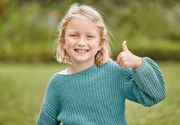 Tout va bien Photo d'une adorable petite fille montrant les pouces vers le haut tout en se tenant dehors