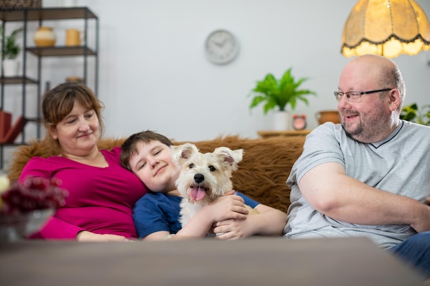 Toute la famille et leur chien sont assis sur le canapé dans le salon et le chien regarde directement dans la caméra