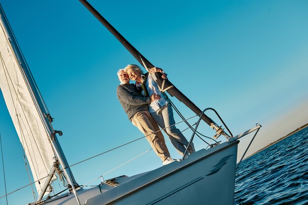 Toute la longueur d'un couple de personnes âgées romantique et heureux debout sur le côté d'un voilier ou d'un pont de yacht