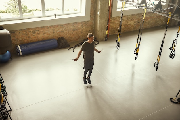 Toute la longueur du jeune homme sportif saute à la corde tout en faisant de l'exercice au gymnase