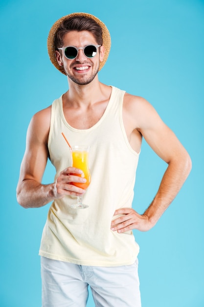 Toute la longueur du joyeux jeune homme debout et tenant un verre de jus d'orange sur le mur bleu