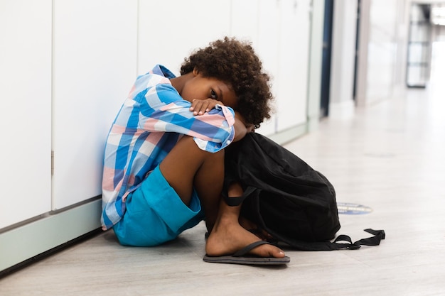 Toute la longueur de l'écolier élémentaire afro-américain assis sur le sol dans le couloir