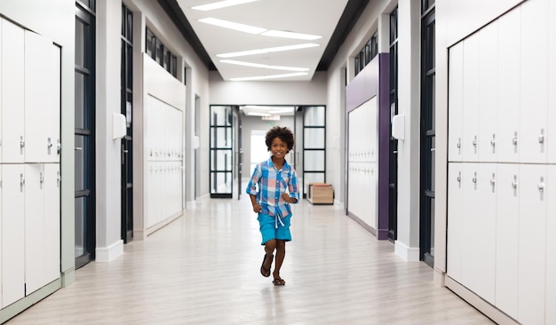 Photo toute la longueur d'un écolier élémentaire afro-américain souriant courant dans le couloir avec des casiers