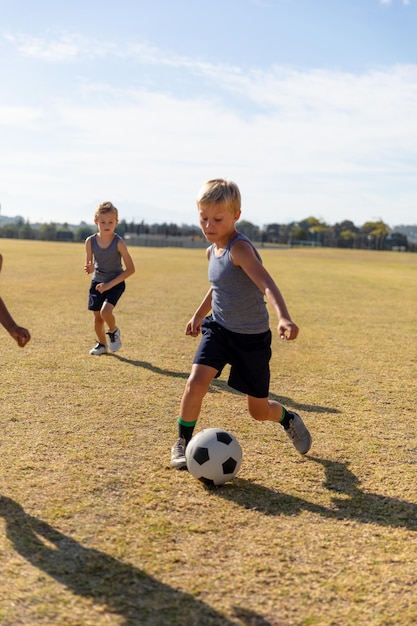 Toute la longueur des écoliers élémentaires caucasiens jouant au football sur le terrain de football contre le ciel