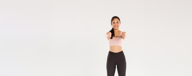 Toute la longueur de l'entraîneur de fitness asiatique beau et mince souriant athlète féminine en vêtements de sport montrant