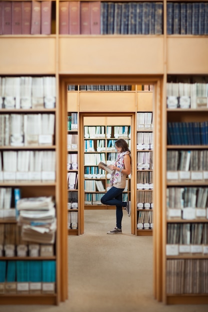 Toute la longueur d&#39;une étudiante en lisant un livre dans la bibliothèque