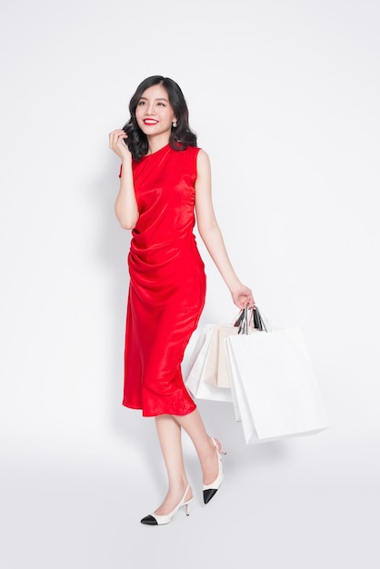 Toute la longueur d'une femme asiatique à la mode joyeuse vêtue d'une robe rouge avec des sacs à provisions