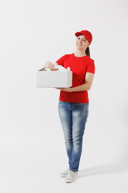 Toute la longueur de la femme au bonnet rouge, t-shirt donnant une boîte à gâteau de commande de nourriture isolée sur fond blanc. Courrier féminin tenant un dessert dans une boîte en carton non marquée. Concept de service de livraison. Réception du colis.