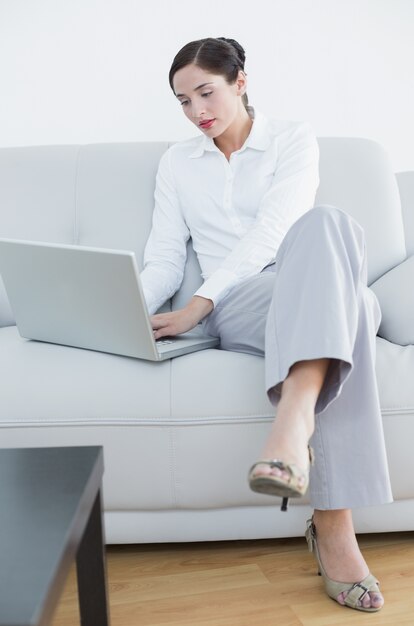 Toute la longueur d&#39;une femme bien habillée en utilisant un ordinateur portable sur le canapé