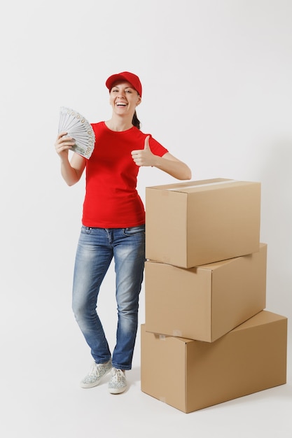 Toute la longueur de la femme de livraison au bonnet rouge, t-shirt isolé sur fond blanc. Courrier féminin près de boîtes en carton vides, liasse de dollars, argent comptant. Réception du colis. Copiez la publicité de l'espace.