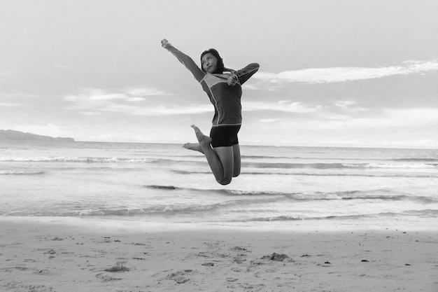 Photo toute la longueur d'une femme sautant sur le rivage sur la plage contre le ciel