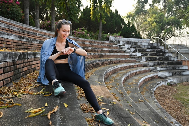 Toute la longueur de la femme sportive vérifiant les résultats de la condition physique ou la fréquence cardiaque sur la smartwatch après avoir couru dans le parc