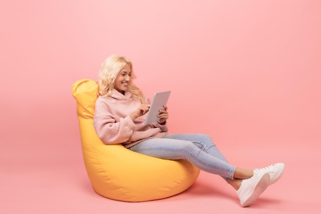 Toute la longueur de la femme utilisant une tablette pc étudiant ou travaillant à distance assis dans un fauteuil poire sur rose