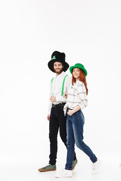 Sur toute la longueur d'un heureux jeune couple portant des costumes, célébrant le jour de la Saint-Patrick isolé sur mur blanc