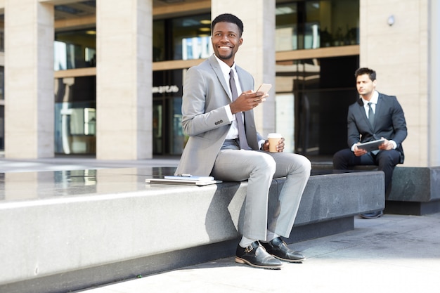 Toute la longueur de l'homme d'affaires assis à l'extérieur en utilisant le téléphone tranquillement