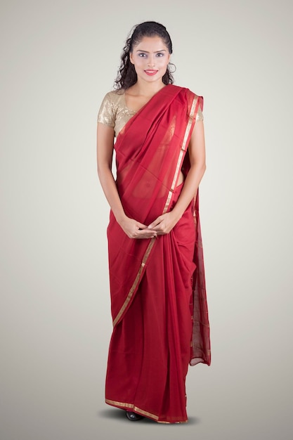 Toute la longueur d'une jeune femme indienne portant un sari rouge et souriant à la caméra. Prise de vue en studio isolée sur fond blanc