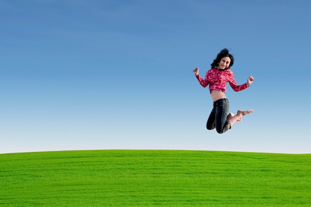 Photo toute la longueur d'une jeune femme sautant sur la terre contre un ciel clair