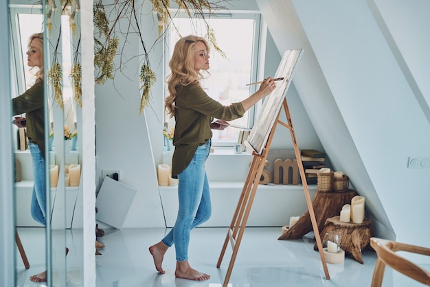 Toute la longueur de la jeune femme séduisante peignant dans un studio d'art