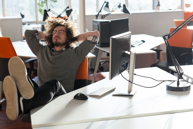 Toute la longueur d'un jeune homme d'affaires décontracté décontracté assis avec les jambes sur le bureau au bureau