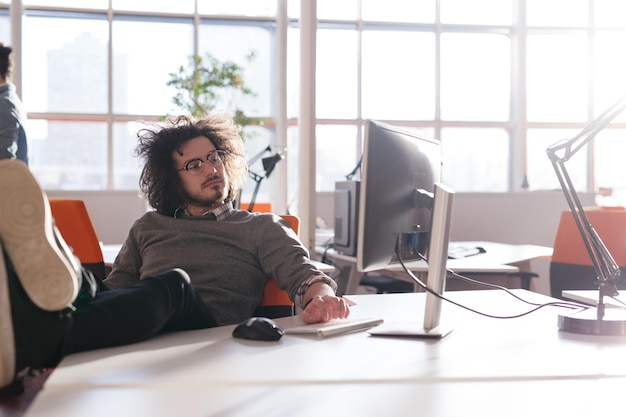 Toute la longueur d'un jeune homme d'affaires décontracté décontracté assis avec les jambes sur le bureau au bureau