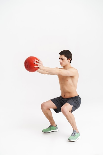 Sur toute la longueur d'un jeune sportif torse nu en forme confiant, faire des exercices avec ballon lourd sur blanc