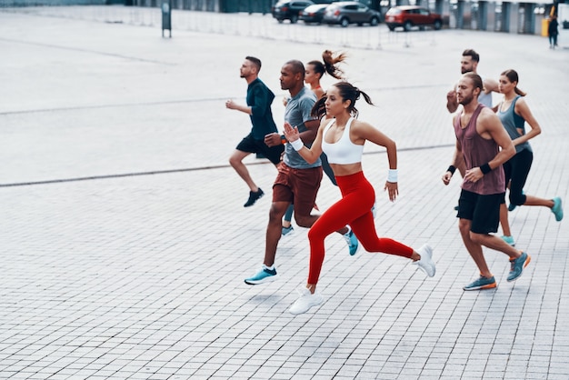 Toute la longueur des jeunes en vêtements de sport faisant du jogging tout en faisant de l'exercice sur le trottoir à l'extérieur