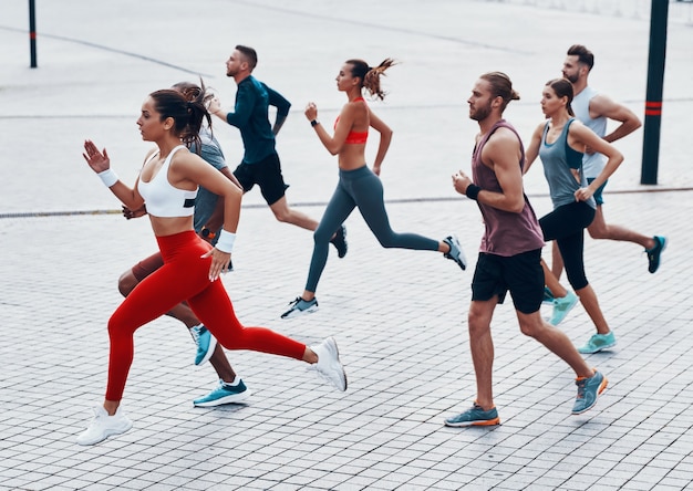 Toute la longueur des jeunes en vêtements de sport faisant du jogging tout en faisant de l'exercice sur le trottoir à l'extérieur