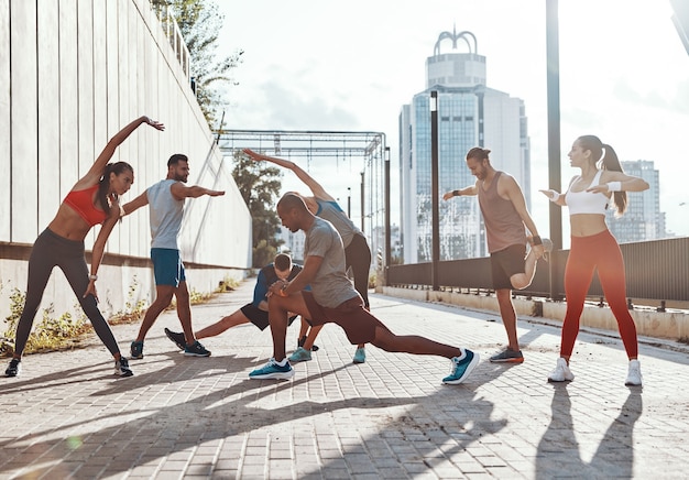 Toute la longueur des personnes en vêtements de sport s'échauffant et s'étirant tout en faisant de l'exercice sur le trottoir à l'extérieur