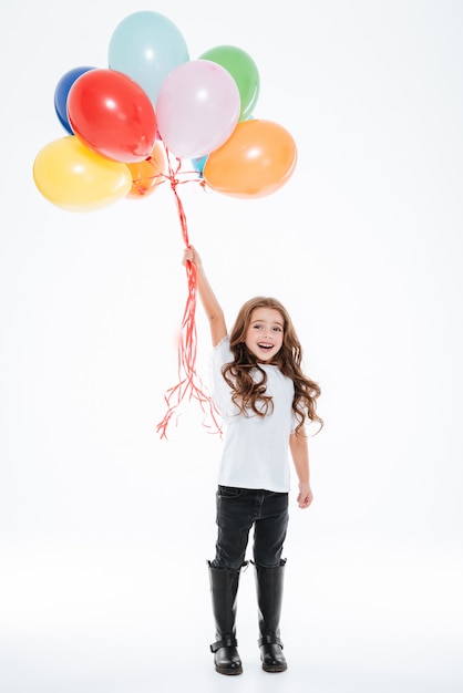 Toute la longueur de la petite fille debout et tenant des ballons colorés