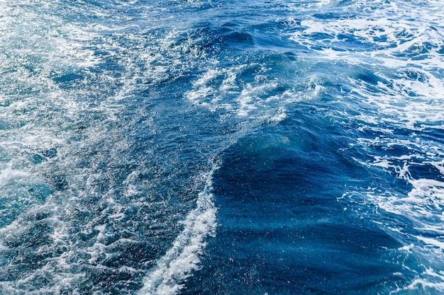 Trace de vague avec de la mousse blanche sur une surface de l'eau derrière un yacht en mouvement rapide