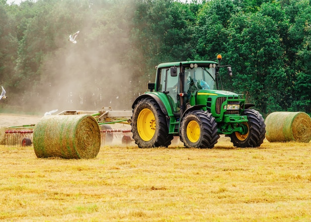 Tracteur, couper le foin en été contre un ciel nuageux bleu, des meules de foin sur le terrain