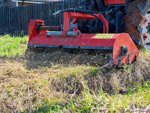 Un tracteur équipé d'une tondeuse broie l'herbe sèche le long de la clôture. Traitement des parcelles