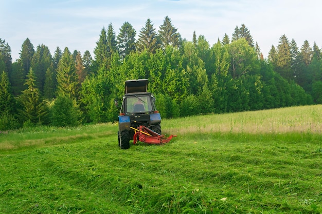 Un tracteur avec une faucheuse portée tond les plantes herbacées des prés