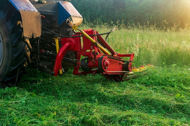 Un tracteur avec une faucheuse portée tond les plantes herbacées des prés