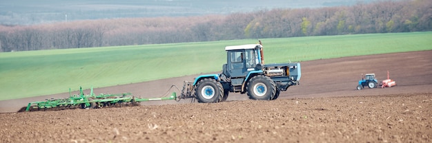 Un tracteur labourant et semant dans le champ. Format panoramique