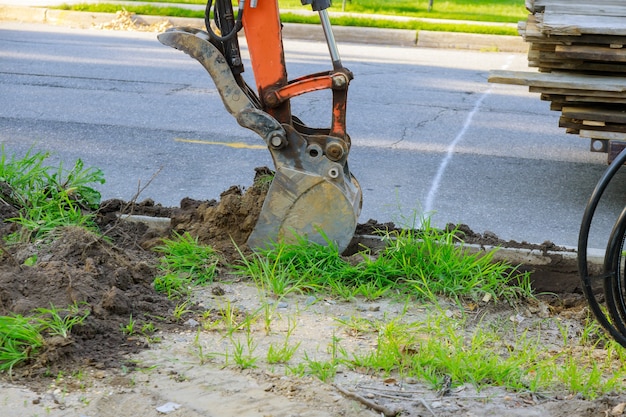 Le tracteur municipal urbain avec louche est de creuser l'égout sur les terrassements.