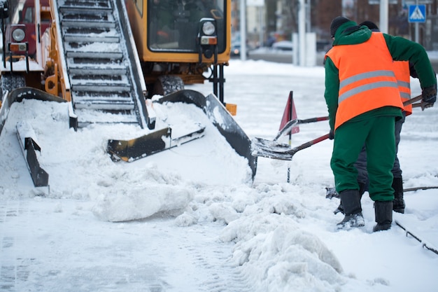 Tracteur nettoyant la route de la neige. Pelle nettoie les rues de grandes quantités de neige en ville. Les travailleurs balaient la neige de la route en hiver, nettoient la route de la tempête de neige.