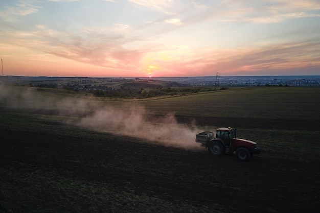 Tracteur pulvérisant des engrais avec des produits chimiques herbicides insecticides sur le terrain agricole au coucher du soleil