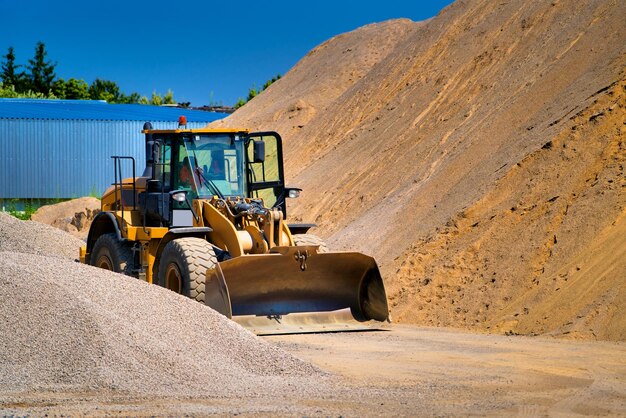 Le tracteur recueille une pelle à gravier extrait du sable et du gravier pour le mélange de béton Ciel bleu au-dessus